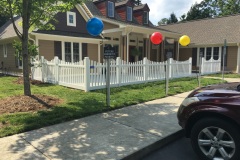 Vinyl fence surrounding a residential property, featuring scalloped design, with colorful balloons and a landscaped yard, showcasing the elegance and durability of Harrison Fence's vinyl fencing solutions.
