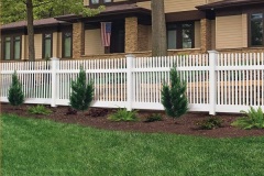 Vinyl fence in white with decorative pickets, enhancing residential property aesthetics and durability, surrounded by green grass and shrubs.