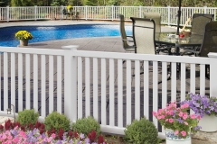Vinyl fencing surrounding a pool area, featuring a white picket design, colorful flower pots, and outdoor seating, illustrating the aesthetic appeal and durability of Harrison Fence's vinyl products.