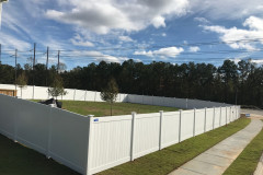 Vinyl fence installation in a residential setting, showcasing a durable and elegant white fence surrounding a grassy area, with trees and a clear blue sky in the background.